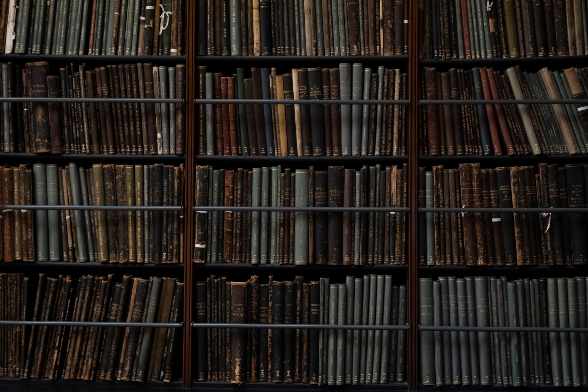 Rayonnages sombres d’une bibliothèque garnis de livres anciens aux reliures usées, maintenus par des barres métalliques.